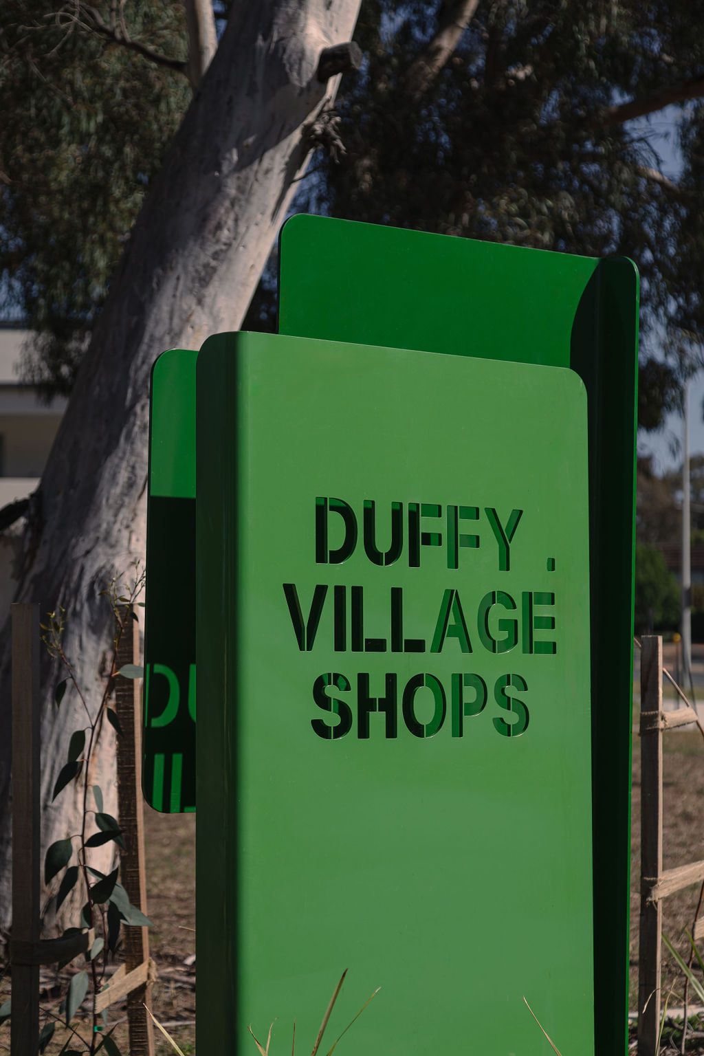 Green Duffy Village Shops sign beside established trees.